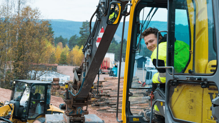 En elev på Bygg- och Maskingymnasiet ler mot kameran från hytten i en grävmaskin.