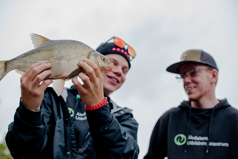 Fiskegymnasiet - två glada sportfiskare där den ena håller upp en nyfångad fisk.