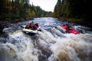 Två båtar fylld med människor som befinner sig mitt i en forsränning. På bilden är det ett gäng elever som paddlar i forsen under en lektion i paddling. En kajak som paddlar i forsen syns också.