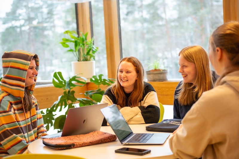 Fyra elever sitter med sina datorer runt ett bord och pluggar.