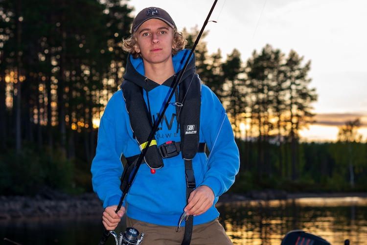 En elev på Fiskegymnasiet står vid en sjö med ett fiskespö.