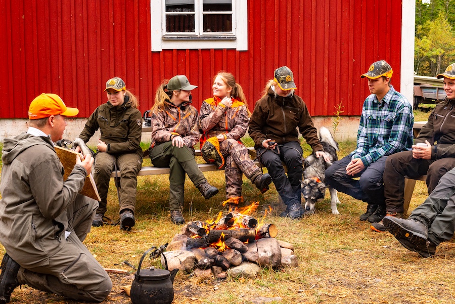 Lektion med Jaktgymnasiet i Älvdalen. Elever sitter vid en brasa och en lärare visar en karta.